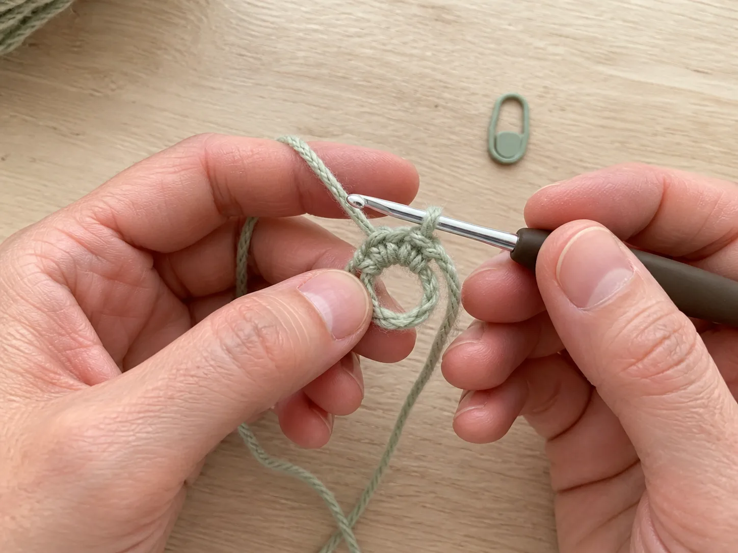 Adult hands crocheting the first small half-double-crochet round into an adjustable yarn ring with a hook.