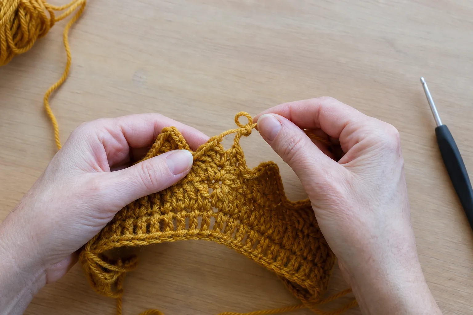 Adult hands carefully undo the most recent round of mustard crochet fabric after finding a count error.