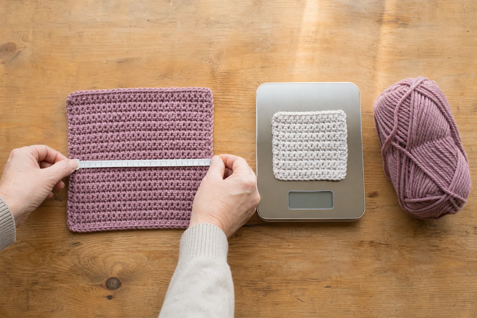 Hands measure a mauve crochet swatch beside a digital scale, a weighed swatch, and matching yarn