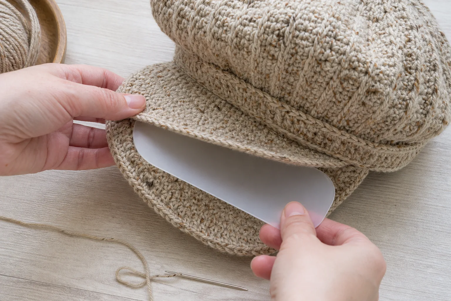 Hands place a smooth rounded flexible visor insert between two crochet layers of a newsboy cap peak
