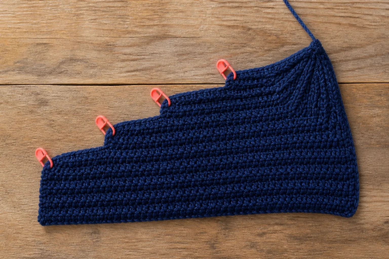 A flat navy crochet wedge uses four coral markers to step toward the crown edge