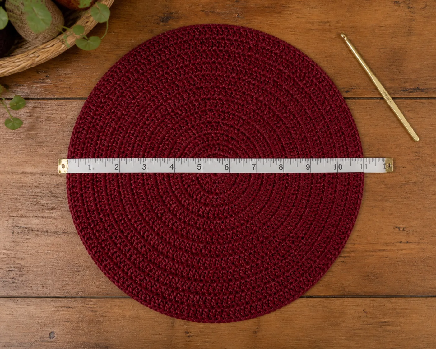 A tape measure spans a flat burgundy crochet beret disc to show where to check its diameter