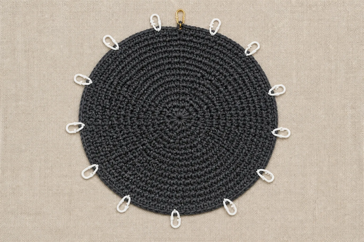 Hands hold a flat charcoal crochet crown with twelve even increase sectors and a gold back marker